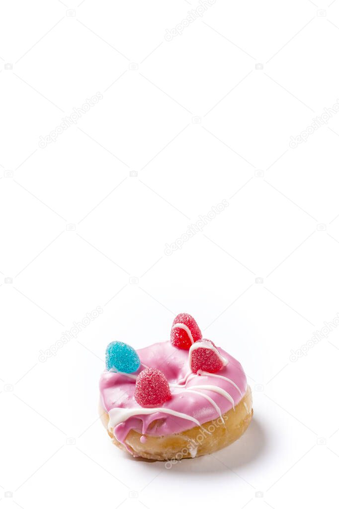 Photograph of a pink donuts painted with white chocolate and decorated with jelly beans.The photo is taken in vertical format on a white background and has copy space.