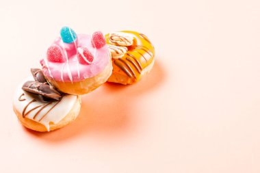 Jelibonla süslenmiş ve çikolatayla çizilmiş 3 çöreğin fotoğrafı. Fotoğraf, krem renkli bir arka planda yatay formatta çekilmiş. Fotoğrafta kopya alanı var..