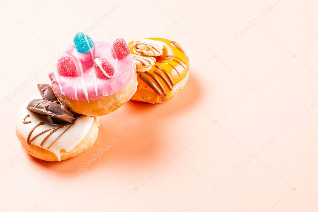 Photograph of 3 donuts decorated with jelly beans and drawn with chocolate.The photo is taken in horizontal format on a cream-colored background.The photo has copy space.