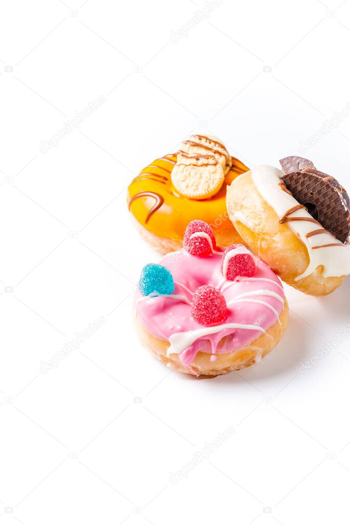 Photograph of three donuts decorated with colored chocolate, cookies and jelly beans.The photograph is taken in vertical format on a white background and has space for advertising.