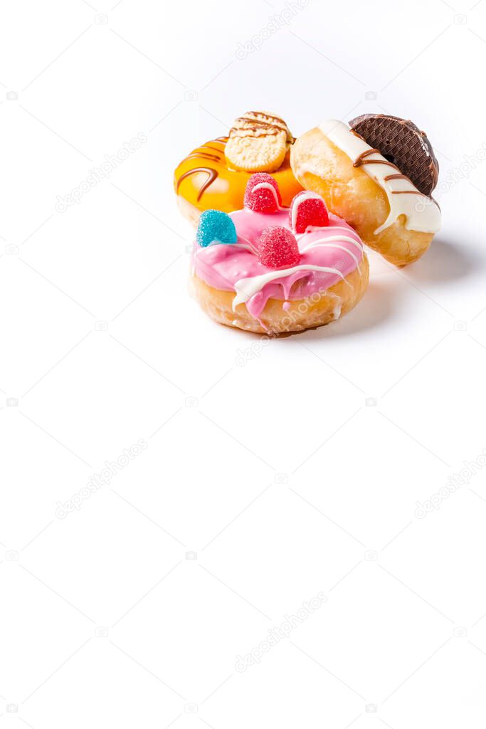 Photo of 3 donuts decorated with colored chocolate, cookies and jelly beans.The photograph is taken in vertical format on a white background and has space for advertising.