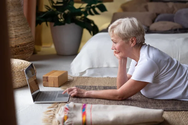 Aktiv senior kvinna surfa på internet på yogamattan. — Stockfoto