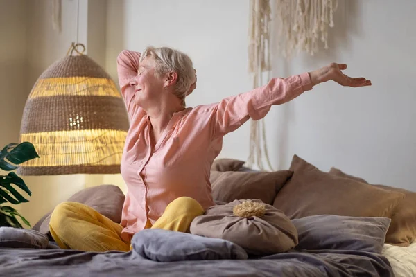 Старша жінка в піжамі посміхається в яскравій вітальні, що розтягується прокидається . — стокове фото