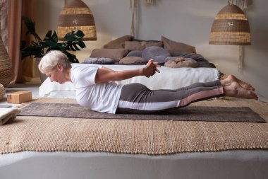 Son sınıf öğrencisi kadın evde yoga yapıyor, Salabhasana ya da Locust pozu veriyor. Sağlık ve sağlıklı yaşam tarzı