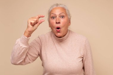 Avrupalı son sınıf öğrencisi kadın elleriyle küçük bir şey gösteriyor. Şaşırtıcı boyutta bir şey gösteriyor. Stüdyo çekimi