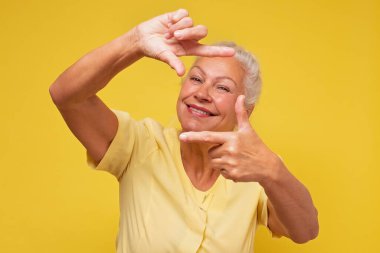 Kıdemli kadın kameraya bakıyor ve el hareketi yapıyor.