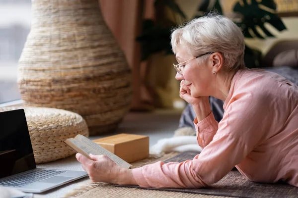 Senior kvinna avkopplande på golvet hemma läsa bok. — Stockfoto