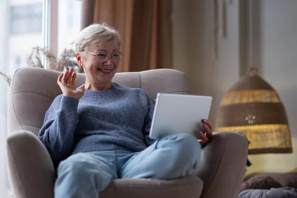 Leende mogen mamma håller i tabletten och viftar med handen hemma. — Stockfoto