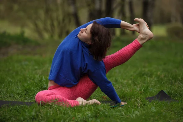 Junge Frau praktiziert Kraunchasana im Park. — Stockfoto