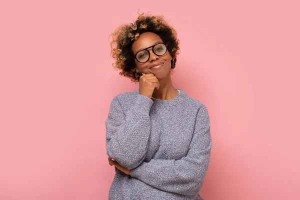 眼鏡をかけセーターを着たアフリカ系アメリカ人の若い女性が笑っている ピンクの壁にスタジオショット — ストック写真