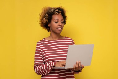 Serbest çalışan ya da çalışan bir öğrenci. Gülümseyen milenyum Afrikalı Amerikalı kadın dizüstü bilgisayarda çalışıyor ya da internette araştırma yapıyor..