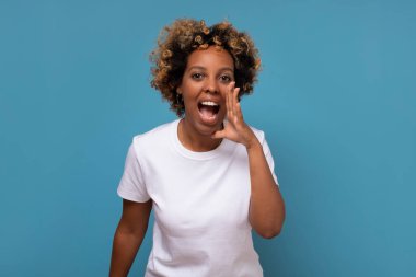 Genç Afrikalı bir kadın elleri ağızda kameraya bağırıyor ve çığlık atıyordu. Son haberleri dinle. Stüdyo resmi mavi duvarda.