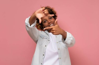 Pembe arka planda izole edilmiş mutlu melez kadın çerçeveli fotoğraf. Yaratıcı fotoğraf konsepti.