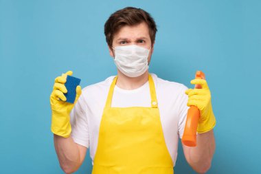 Önlüklü, koruyucu maskeli ve eldivenli genç adam Coronavirus 'tan her şeyi temizlemeye hazır..