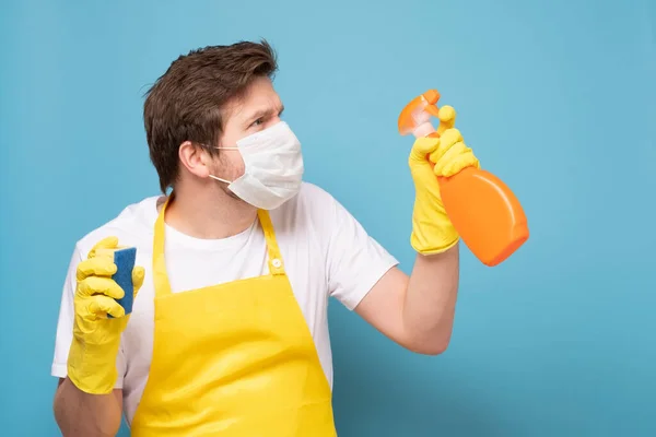 Young seious man in apron, protective mask and gloves ready to clean everything from coronavirus.