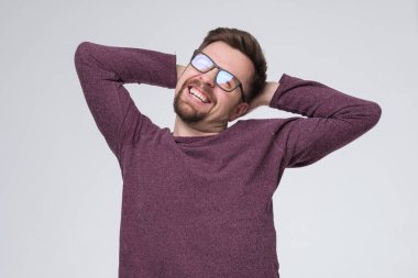 Sakallı, süveter giyen, gözlüklü, gevşeyen, esneyen, kolları ve elleri başının arkasında olan bir adam.