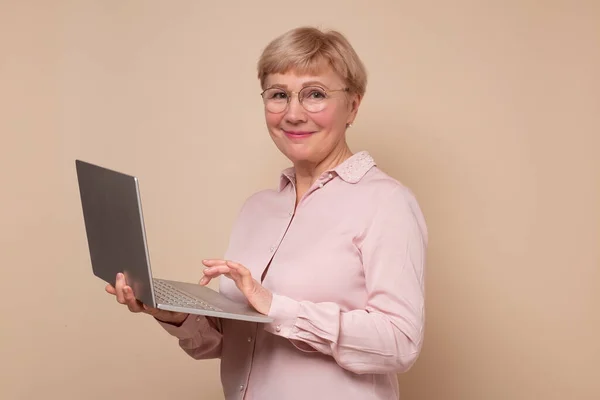 Веселая взрослая женщина, стоящая с ноутбуком и улыбающаяся. — стоковое фото