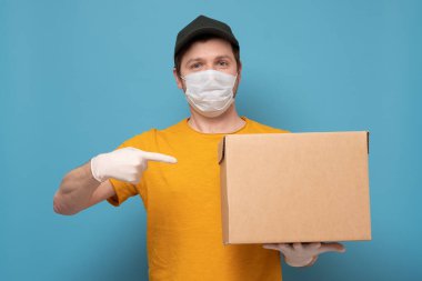 Teslimatçı elinde plastik eldiven ve maskeyle karton kutu tutuyor.