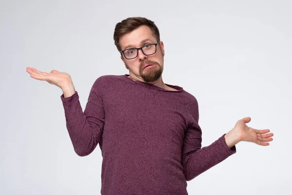 Young confused man shrugging shoulders, spreading hands isolated on pink background — Stock Photo, Image