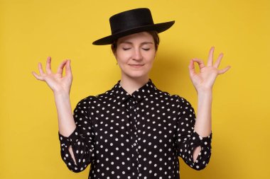 Minnettar beyaz kadın siyah şapkalı, meditasyon yaparken gülümsüyor.