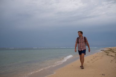 Beyaz adam kumlu sahilde yürüyor Bali 'de okyanusa bakıyor