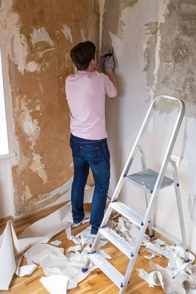 Homem caucasiano arrancando velho papel de parede da parede se preparando para a redecoração de casa — Fotografia de Stock