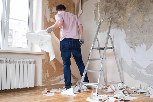 Caucasian man tearing off old wallpaper from wall preparing for home redecoration — Stock Photo, Image