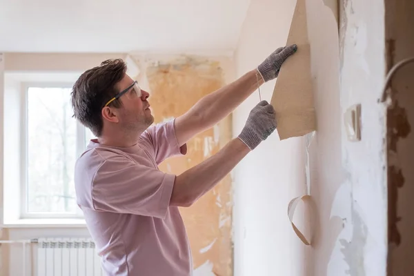 Caucasian man tearing off old wallpaper from wall preparing for home redecoration — Stock Photo, Image