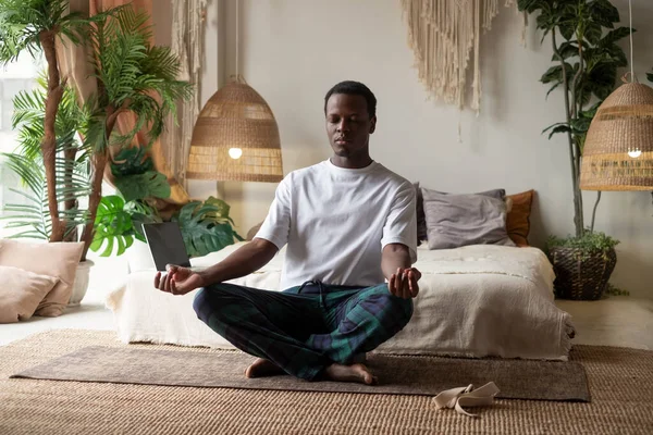 Young african man meditating sitting at his bedroom in the morning Stock Image