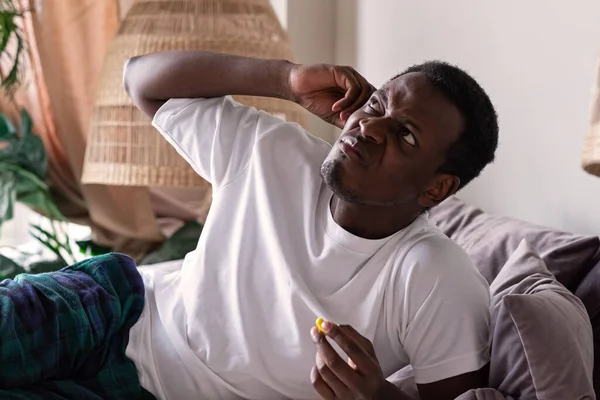 Раздражённый африканский молодой человек вставляет затычки для ушей — стоковое фото