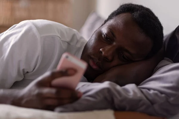 Smutný africký muž ležící v posteli čtení sms od své přítelkyně — Stock fotografie