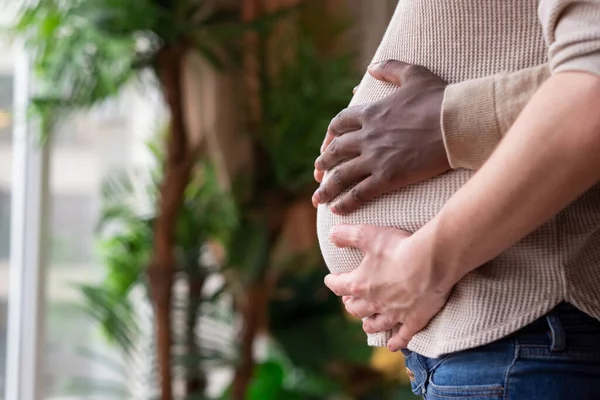 Zwarte aanstaande vader die de buik van zijn blanke zwangere vrouw vasthoudt. Gemengd huwelijk. — Stockfoto