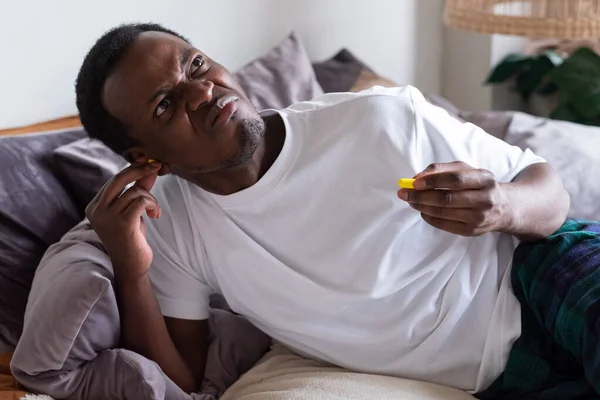 Joven africano molesto insertando tapones para los oídos —  Fotos de Stock