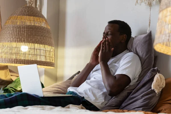 Cansado homem africano bocejando em casa na cama. — Fotografia de Stock