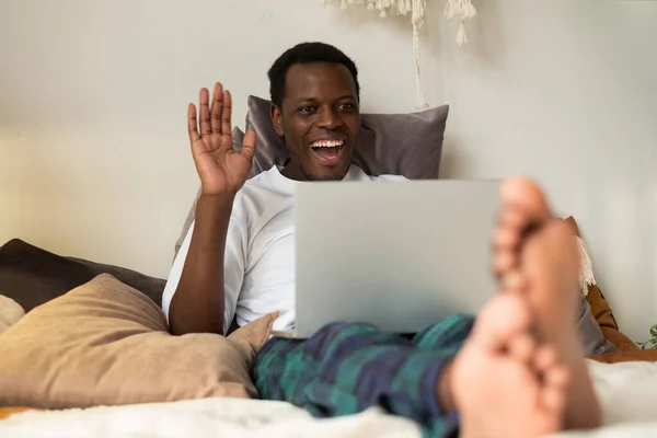 Homem preto com tablet descansando na cama cumprimentando mão acenando. — Fotografia de Stock