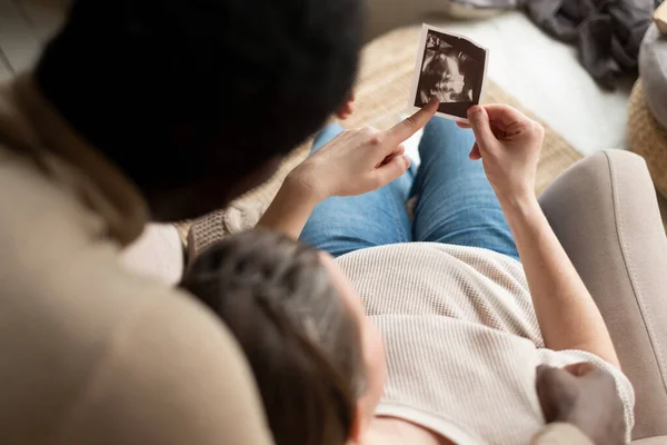 Woman holding ultrasound image of her baby showing her husband details on it. — Stock Photo, Image