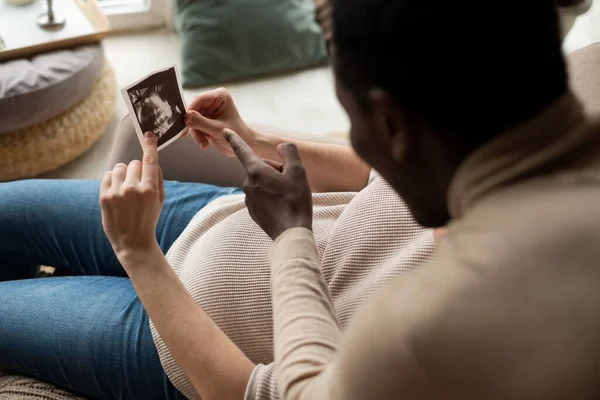 Женщина, держащая ультразвуковое изображение своего ребенка, показывает на нем данные своего мужа.. — стоковое фото