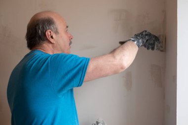 Macun bıçağıyla duvarları sıva yapan yaşlı adam.