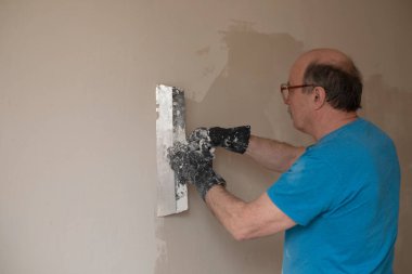 Macun bıçağıyla duvarları sıva yapan yaşlı adam.