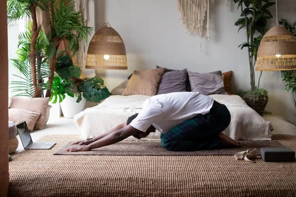 African man doing yoga at home, having rest in balasana or child pose, relaxing body muscles between asana