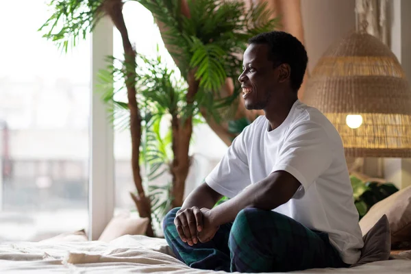 Positive young smiling african man sitting on bed at the morning. — стоковое фото