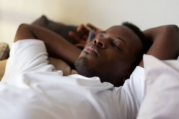 Snygg etnisk svart afrikansk man vilar i sängen sover eller sover. — Stockfoto