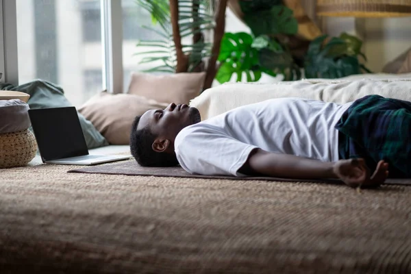 Yoga. African young man meditating on a floor and lying in Shavasana pose. Royalty Free Stock Photos