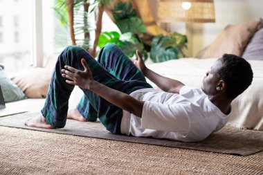 Evde yoga yapan bir adam Bot Poose ya da Paripurna Navasana yapıyor.
