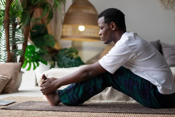 Африканский юноша, сидящий в позе пасхимоттанасаны или интенсивной дорсальной растяжки, сидящий впереди позы изгиба — стоковое фото