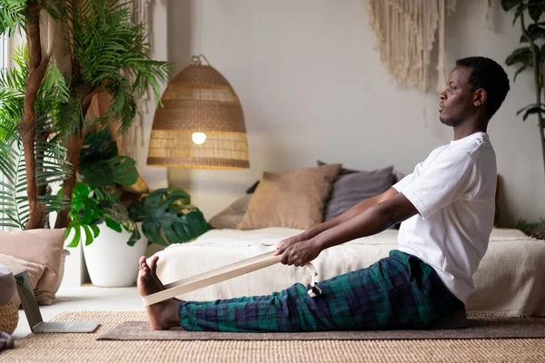 African young man sitting in paschimottanasana or Intense Dorsal Stretch pose, seated forward bend posture Stock Photo