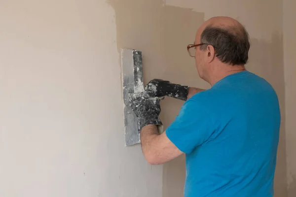 Hombre mayor con cuchillo de masilla yeso reparación de la pared — Foto de Stock