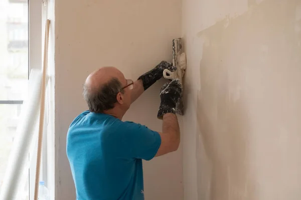 Hombre mayor con cuchillo de masilla yeso reparación de la pared — Foto de Stock