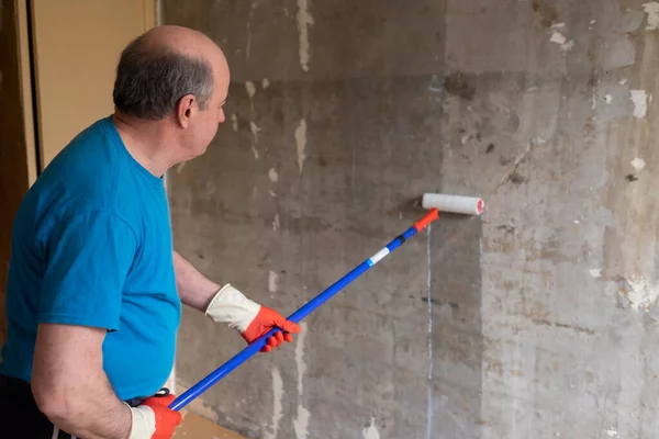 Hombre pintando paredes de cemento usando rodillo cepillo y cebador haciendo una renovación. — Foto de Stock