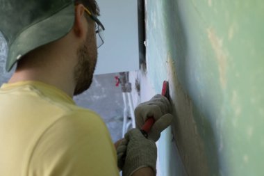 Kafkasyalı adam eski boyayı kazıyıcı aletle temizliyor..